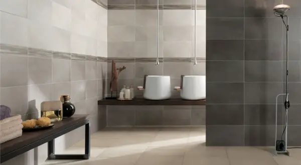 Bagno moderno con lavabi sospesi e piastrelle a diverse altezze, che creano un effetto visivo dinamico.