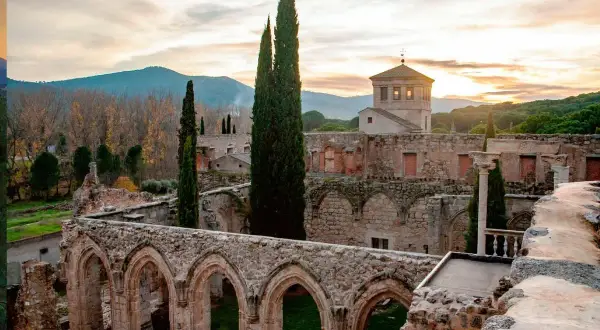 Ruinas de antiguos monasterios cerca de Madrid, con arcos de piedra y cipreses altos bajo un cielo crepuscular.
