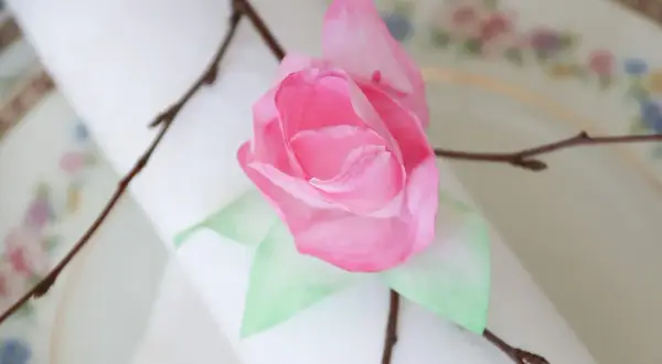 En rosa ros av blommor av kaffefilter, dekorerad med en kvist på en duk.