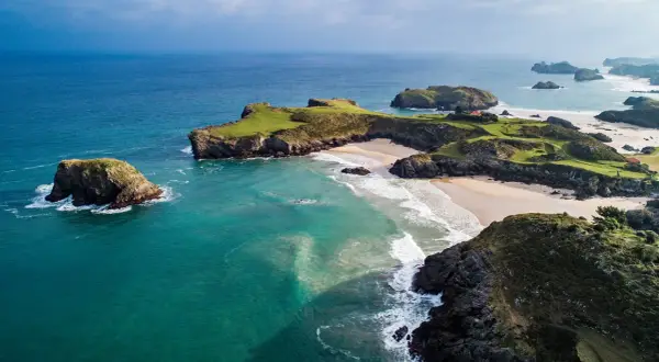 Impresionante vista aérea de la ruta costa Asturias en coche. Playas doradas, acantilados verdes y el mar turquesa crean un paisaje idílico.