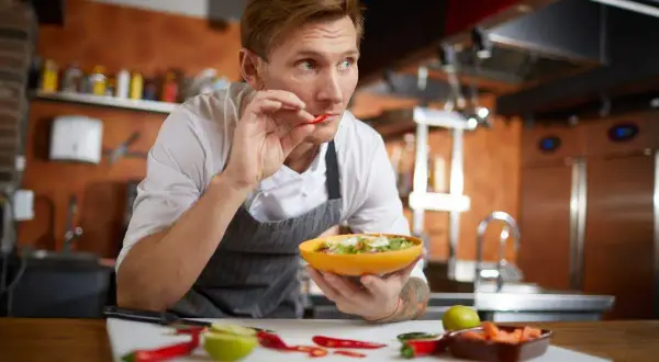 Koch probiert Chili, um scharf essen zu trainieren. Er hält eine Schüssel mit Salat und prüft die Schärfe.