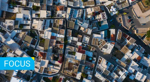 Vista aerea di un villaggio con tetti bianchi e colorati. Un tetto rovescio, con tegole rosse, spicca tra gli altri.