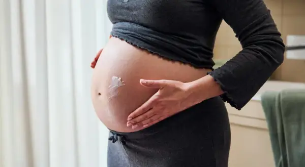 Gravid kvinna smörjer in sin mage med kräm för att motverka torr hud.