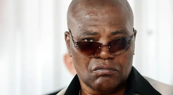 Arron Pryor, a man with a serious expression, wears stylish sunglasses and a light-colored jacket with a black collar.