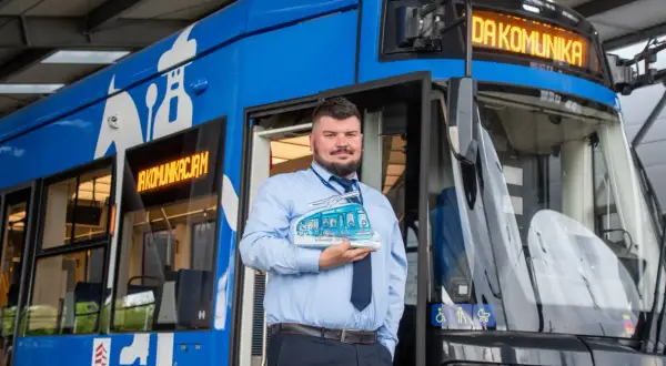 Pracownik MPK trzymający model tramwaju przed niebieskim pojazdem. To symbol publiczny transport krakow.