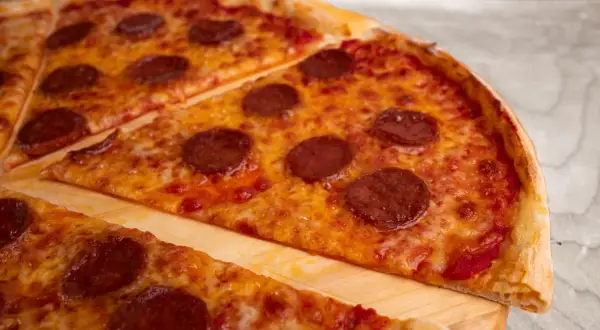 Kawałki pizzy pepperoni z roztopionym serem na desce.