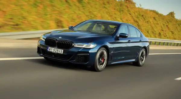 Ciemnoniebieskie BMW 545e pędzi autostradą, otoczone zielenią.
