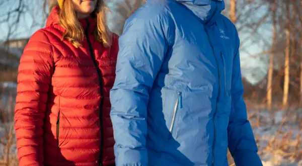 Två personer i vinterkläder, en i röd och en i blå, varmaste dunjackan, står utomhus i snö.