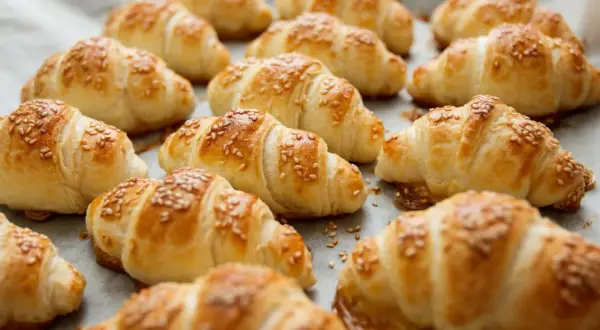 Croissant dorati e fragranti, preparati con pasta sfoglia e cosparsi di semi di sesamo, pronti per essere gustati.