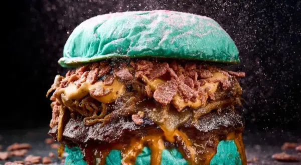 Una hamburguesa gigante con pan azul, carne jugosa, queso derretido y crujiente tocino, perfecta para un festival hamburguesa.