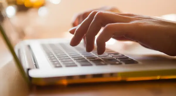 Mani che digitano su un laptop, con luci sfocate sullo sfondo. Un'istantanea del **mod ap 70** che cattura la concentrazione.