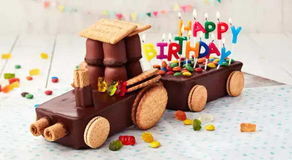 Schokoladen-Traktor-Torte, die man leicht selber machen kann, mit bunten Kerzen und Gummibärchen verziert.