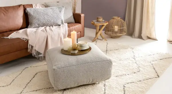 Gemütliches Wohnzimmer im hygge stil mit Ledersofa, Kissen, Decken, Kerzen und einem Teppich.