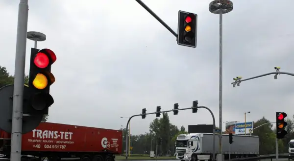 Na skrzyżowaniu widać czerwone i żółte światła. Białe kamery nad światłami monitorują ruch.