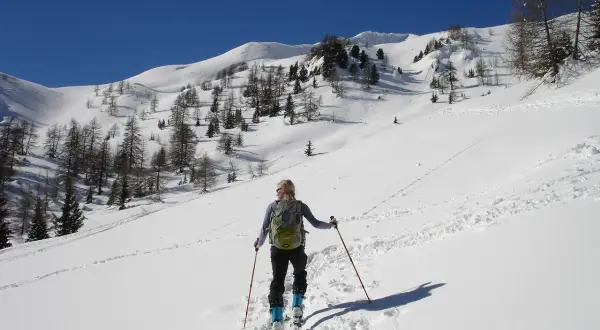 Sciatrice con zaino e bastoncini, in un paesaggio innevato con alberi radi e montagne sullo sfondo. La **forca canapine** è il suo obiettivo.