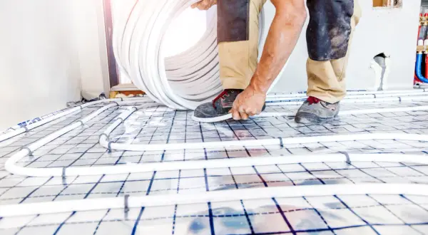 Worker installing underfloor heating pipes on a grid system.
