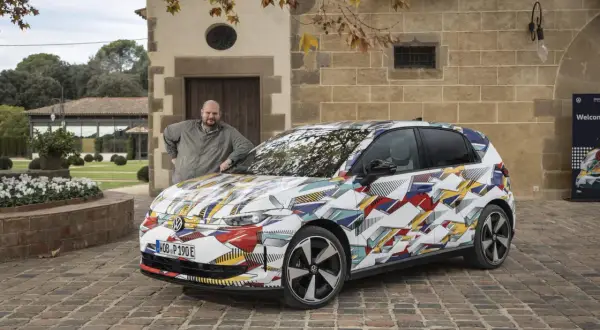 Man lutar sig mot en Volkswagen ID.2 med ett färgglatt, geometriskt mönster.