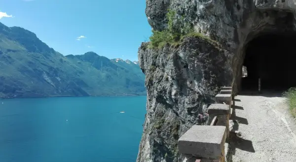 Sentiero panoramico per trekking a Riva del Garda, con vista sul lago e un tunnel scavato nella roccia.
