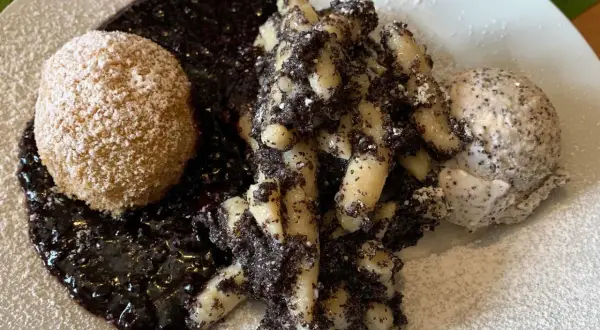 Gedrehte Nudeln mit Mohn, eine Kugel und Beerensoße, bestäubt mit Puderzucker.