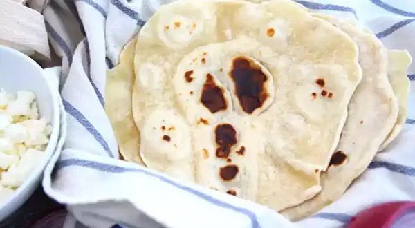 Färska tortillabröd, perfekta för ditt nästa tortilla recept. Bredvid syns skålar med tillbehör som ost och lök.