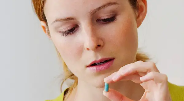 Kobieta zamyślona trzyma niebieską kapsułkę, być może benzodiazepiny, zastanawiając się nad jej przyjęciem.
