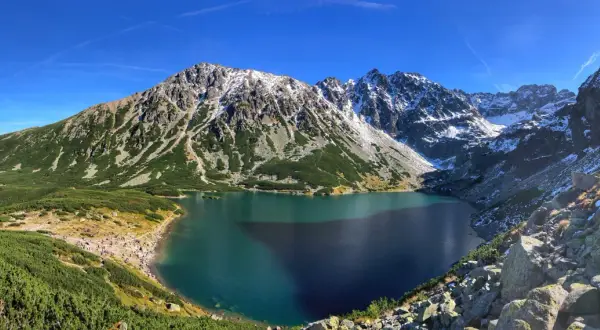 Piękne Tatry dla początkujących: Morskie Oko otoczone zielenią i ośnieżonymi szczytami. Tłumy turystów podziwiają widok.