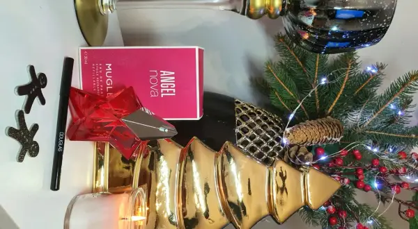 Świąteczna kompozycja z perfumami Angel Nova Mugler 50 ml, świecą, choinką i ozdobami.