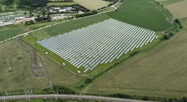 Widok z lotu ptaka na dużą farmę paneli słonecznych otoczoną polami i linią kolejową.