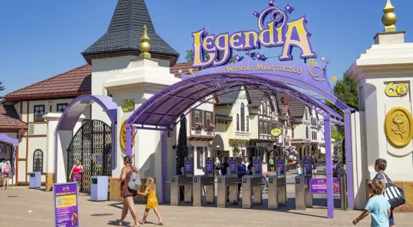 Wejście do Legendii, jednego z parków rozrywki w Polsce. Rodziny wchodzą przez bramki pod fioletowym łukiem z napisem "LegendiA".