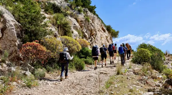 Un groupe de randonneurs explore un sentier rocailleux en Sardaigne, entouré de végétation méditerranéenne et de falaises.