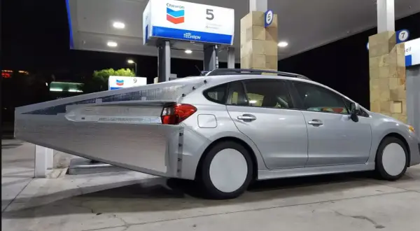 Silverbil med en stor, silverfärgad aerodynamisk förlängning bak. En uppfinning för att spara bensin vid en Chevron-mack.