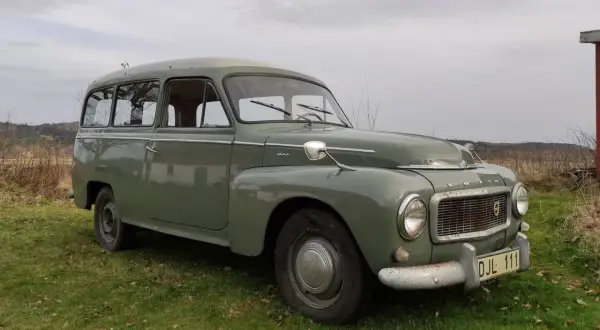 Grön Volvo P210 parkerad på en gräsmatta. Bilen har en klassisk design och ser ut att vara i gott skick.