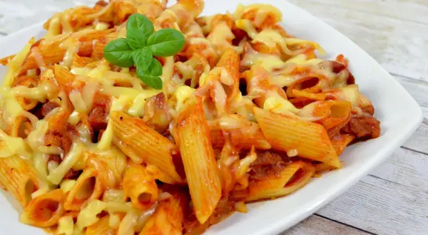 Penne z sosem pomidorowym i kawałkami pikantnego chorizo, zapieczone pod ciągnącym się serem. Udekorowane listkiem bazylii.