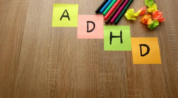 Kolorowe karteczki z literami A, D, H, D układają się w napis ADHD. Obok leżą flamastry i pomięte kartki.