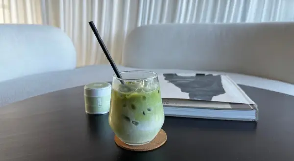 Un verre de lait matcha glacé, parfait pour profiter des bienfaits du matcha. Une petite boîte de matcha est à côté.