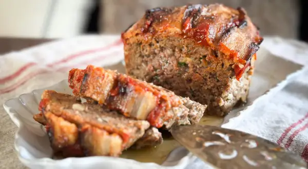 Un délicieux pain de viande, garni de tomates et de lardons, est servi sur une assiette blanche.