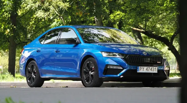 Błękitna Skoda Octavia RS 2025 z czarnymi felgami, zaparkowana wśród zieleni.