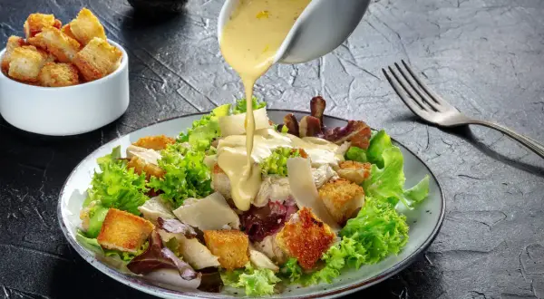 Sałatka cezar oryginalny przepis: chrupiące grzanki, kurczak i parmezan polane kremowym sosem.