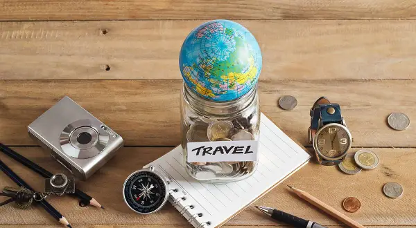 Bocal rempli de pièces avec un globe, un appareil photo, une boussole et un carnet, prêt pour le backpacking en Europe.