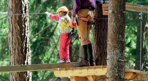 Bambina con casco giallo e adulto su passerella in un parco avventura Marche.