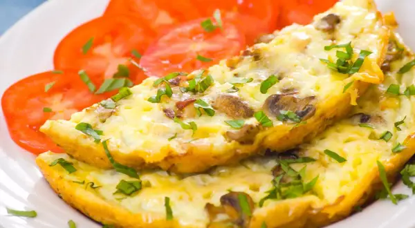 Puszysty omlet z pieczarkami i natką pietruszki, podany z plastrami pomidora. Idealne śniadanie.