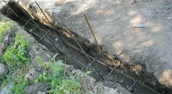 Zbrojenie do fundamentu ogrodzeniowego w wykopie. Metalowe pręty tworzą siatkę, gotową na zalanie betonem.
