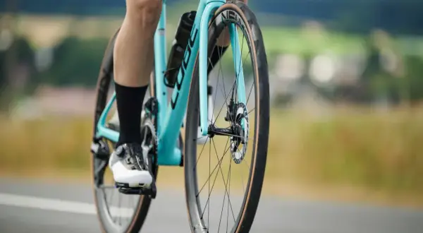 Radfahrer auf einem hellblauen Rennrad mit breiten Reifen fährt auf einer Straße.