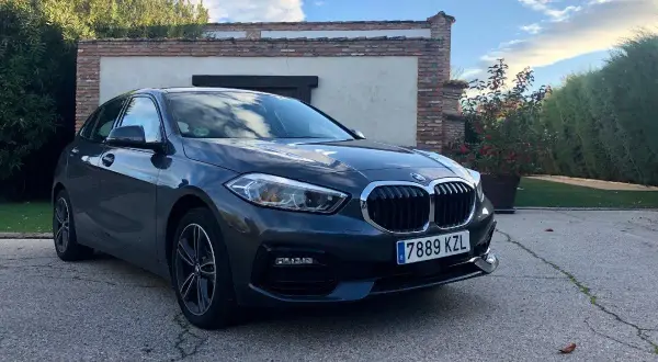 Un BMW Serie 1 116d gris aparcado frente a una casa con vegetación. A pesar de su aspecto, este modelo puede presentar problemas.