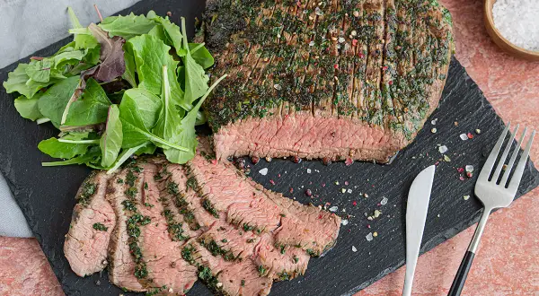 Saftiges Flank Steak, mariniert und perfekt gegrillt, mit frischem Salat und Gewürzen auf einem Schieferbrett serviert.