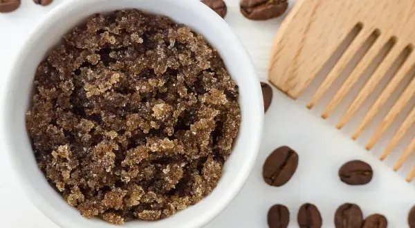 Domowy peeling do skóry głowy z kawy w białej miseczce, obok drewniany grzebień i ziarna kawy.