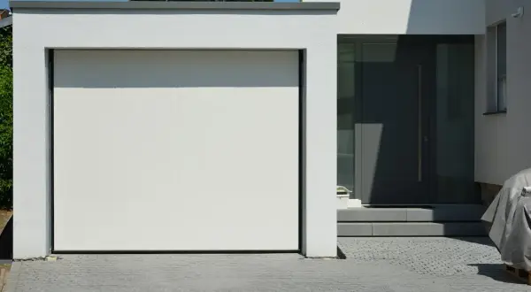 Moderne grenzbebauung mit weißer Garagentür und dunkler Eingangstür. Gepflasterte Einfahrt.