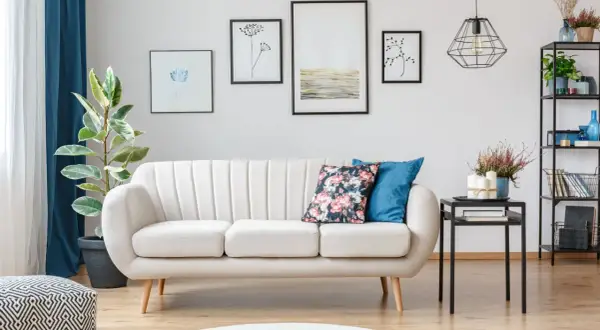 Jasna sofa na nóżkach ułatwia sprzątanie robotem, bo wjedzie pod nią. Wady i zalety tej konfiguracji widać na drewnianej podłodze.