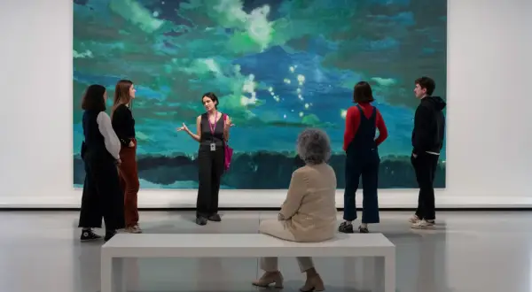 Visite guidée d'une œuvre d'art abstraite aux teintes bleues et vertes, évoquant une scène céleste. Un groupe écoute attentivement, comme à la bourse du commerce.