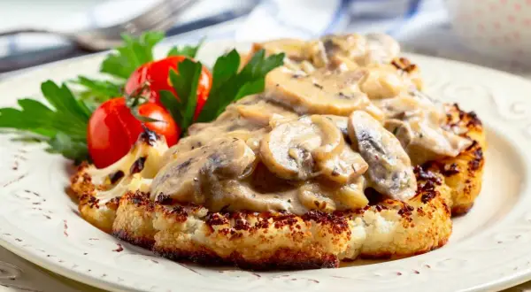 Grillowany kalafior w sosie grzybowym z pomidorkami i natką pietruszki na talerzu.